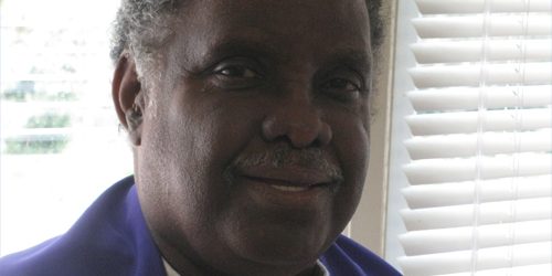 A man stands in front of a window. He is smiling and backlit by a bright day.