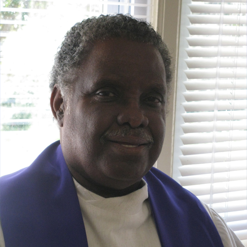 A man stands in front of a window. He is smiling and backlit by a bright day.